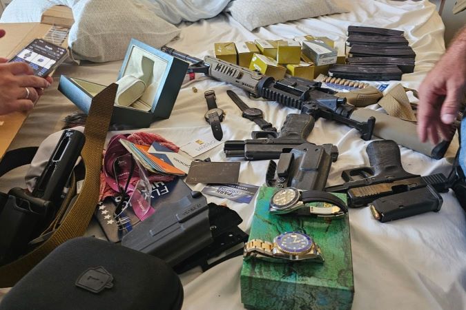 Imagem de armas, munição, relógios, em cima da cama.
